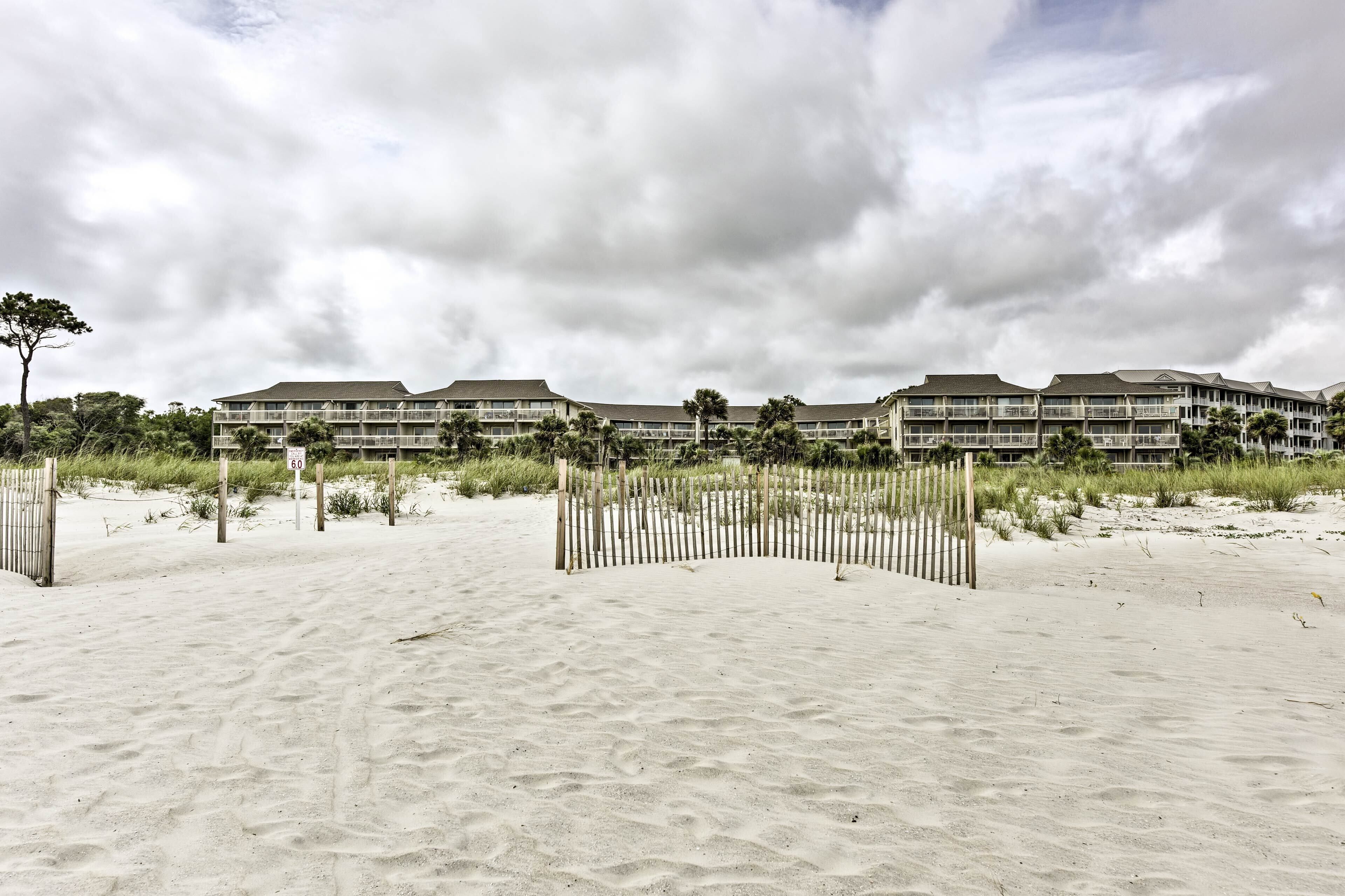 A beachfront hotel with multiple buildings, a sandy beach, and a wooden fence.