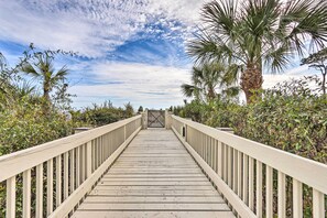 A wooden boardwalk leading to a gate, surrounded by lush greenery and palm trees. - Walk to Bars & Shops: Resort Condo in Hilton Head! (Hilton Head Island)