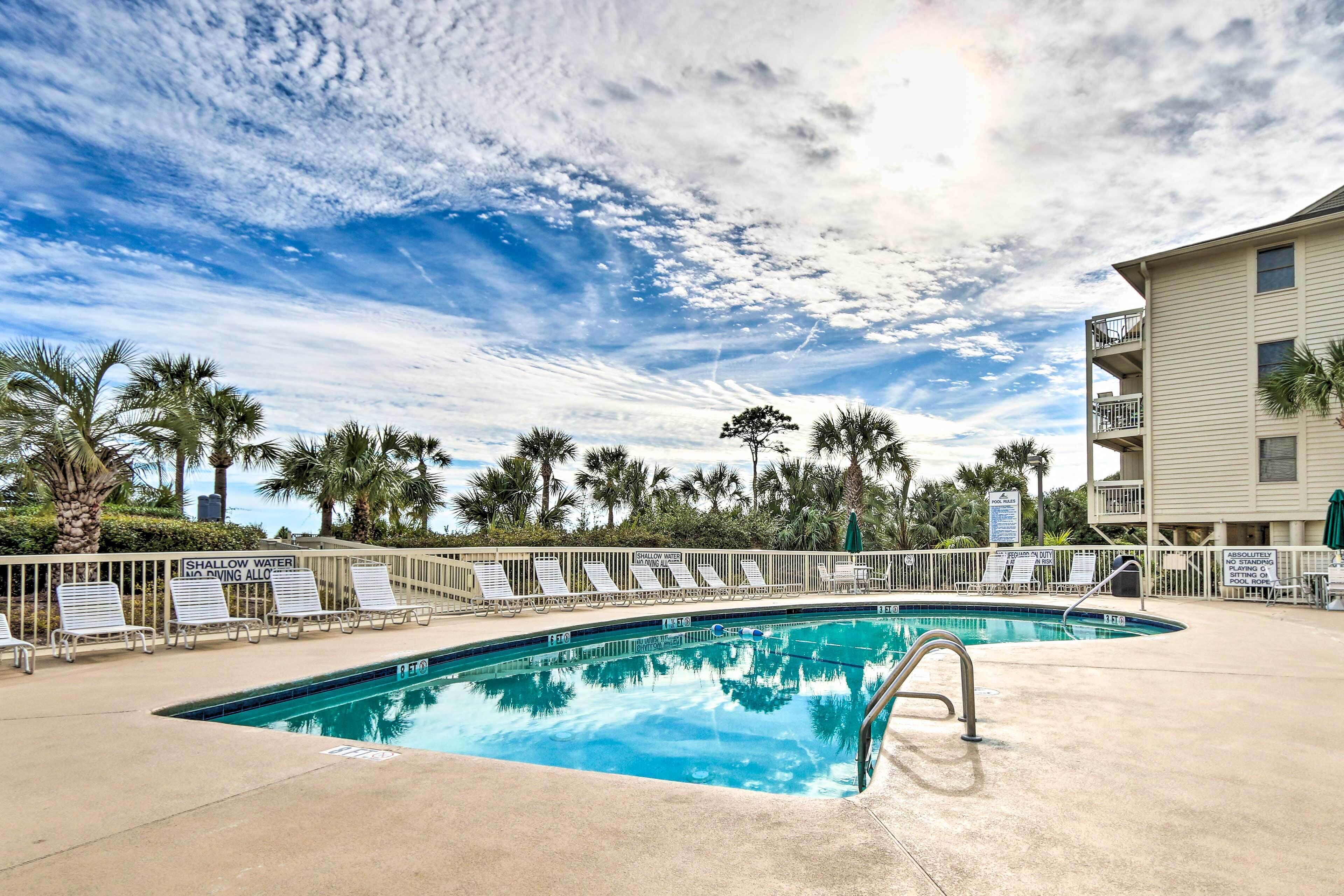 A swimming pool with lounge chairs, palm trees, and a building with balconies.