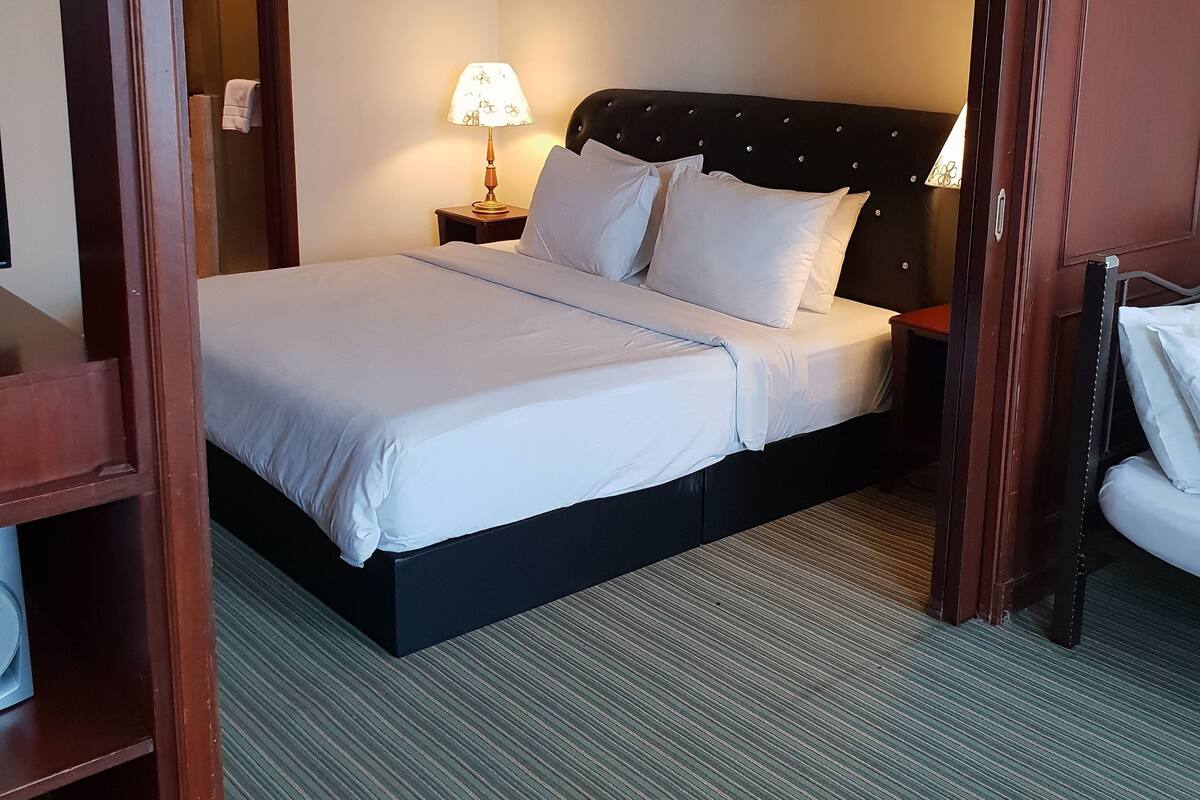 Une chambre d’hôtel avec un grand lit, une table de chevet avec une lampe, un tableau au mur et un cadre de porte en bois.