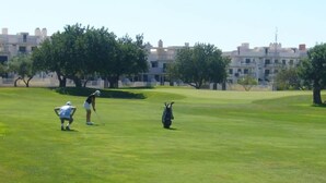 Un parcours de golf avec un green d’entraînement, des arbres et des bâtiments en arrière-plan.
