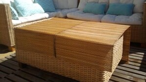 Un canapé en osier avec des coussins, un pouf assorti et une terrasse en bois.