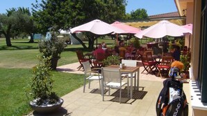 Un espace extérieur aménagé en terrasse, avec des tables et des chaises sous des parasols, un sac de golf et une plante en pot.