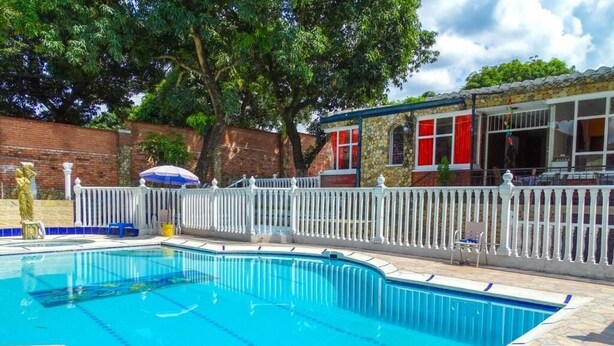 A swimming pool with a white fence, a covered seating area, and a brick wall in the background. - Hotel La Gran Mansion De La Negra (Melgar)