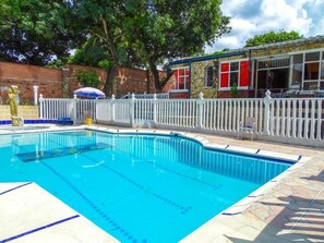 Una piscina con recinzione bianca, una zona relax coperta e un muro di mattoni sullo sfondo.