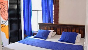A hotel room with a bed, blue curtains, and a wooden headboard. - Hotel La Gran Mansion De La Negra (Melgar)