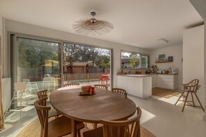 Une cuisine moderne dotée d’un grand îlot central, de portes-fenêtres coulissantes donnant sur un espace extérieur et d’une table à manger avec des chaises.
