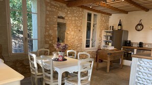 Una cocina de piedra rústica con zona de comedor, sillas blancas y una mesa.