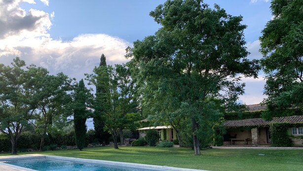 Piscina rectangular con cubierta de madera, rodeada de césped cuidado y árboles.