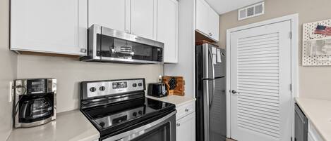 A kitchen with white cabinets, a stainless steel range, a coffee maker, and a refrigerator.