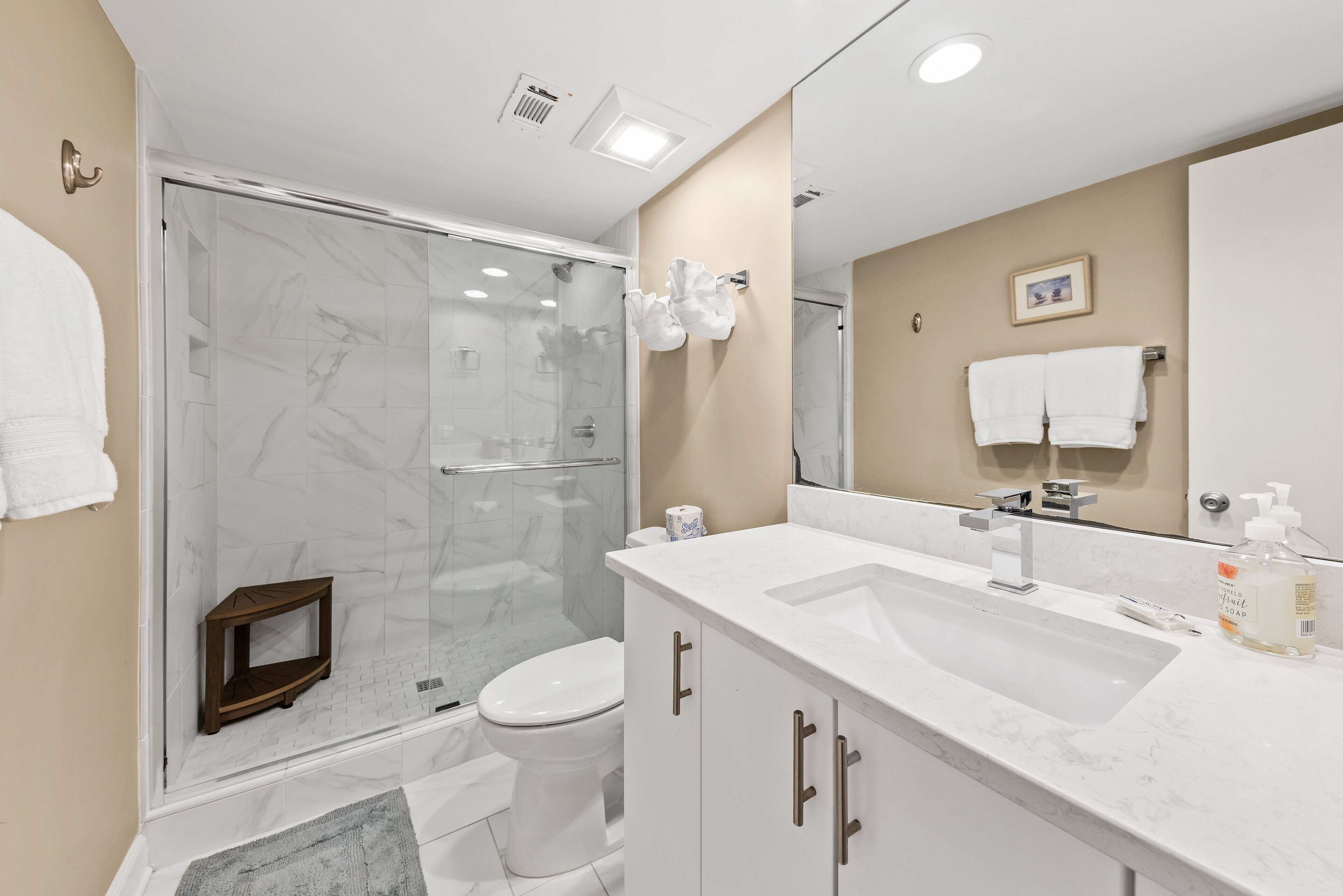 A modern bathroom with a glass-enclosed shower, a white sink, and a large mirror.