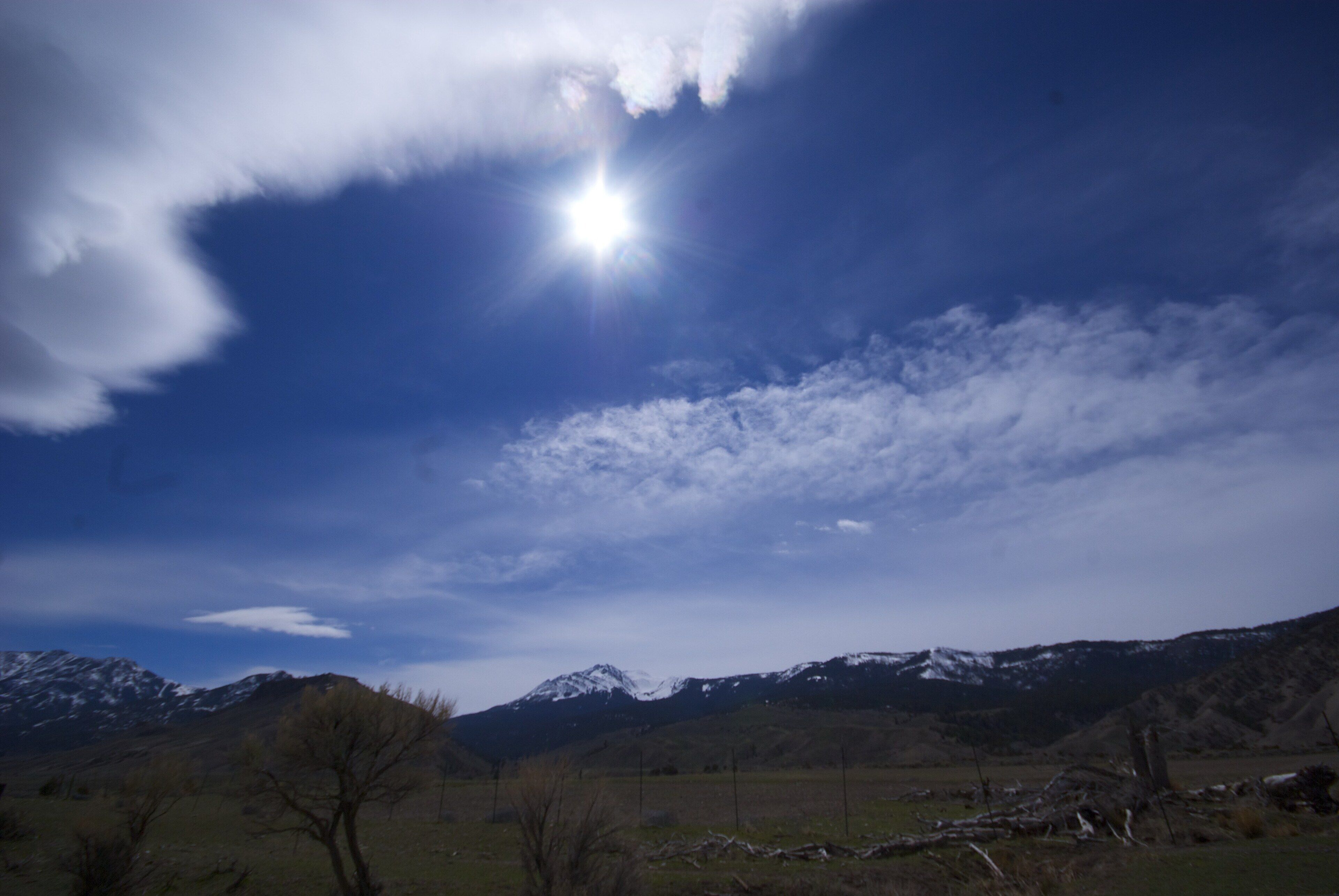 Un paisaje montañoso con cielo despejado y el sol brillando entre las nubes.