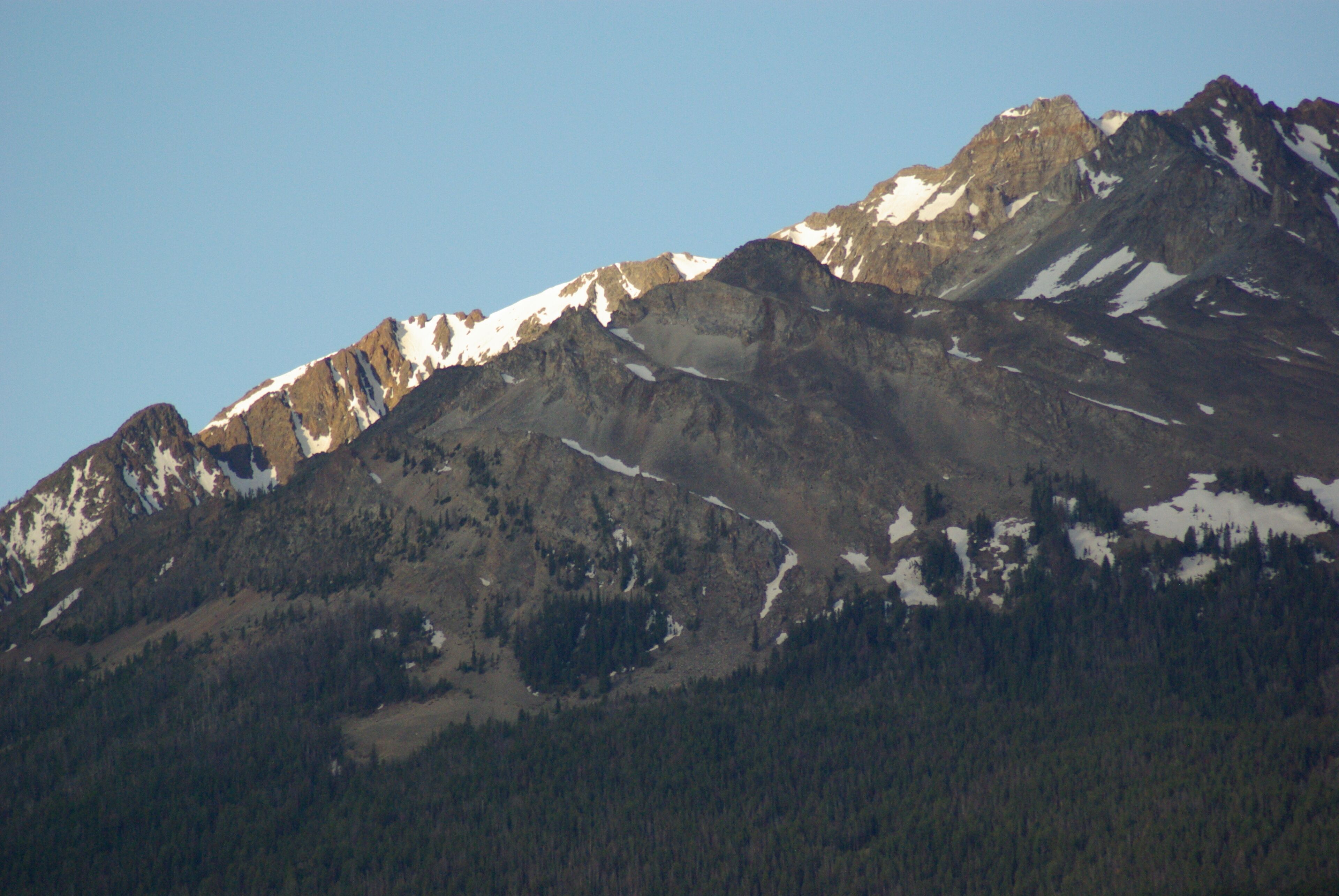 A mountain range with snow-capped peaks and dense forested areas.