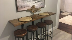 A wooden bar stool set with a woven placemat, a framed painting of a beach scene, and a rustic wooden piece on the wall. - Charming Cottage in Fabulous Location in Niagara on the Lake (Niagara-on-the-Lake)