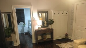 A living room with a fireplace, a sofa, a coffee table, a lamp, a console table with a mirror, and a door with hooks. - Charming Cottage in Fabulous Location in Niagara on the Lake (Niagara-on-the-Lake)