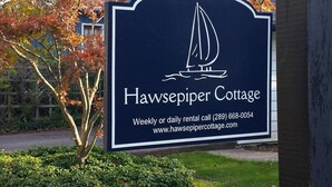 A sign for Hawsepiper Cottage with a sailboat logo, contact number, and website. - Charming Cottage in Fabulous Location in Niagara on the Lake (Niagara-on-the-Lake)