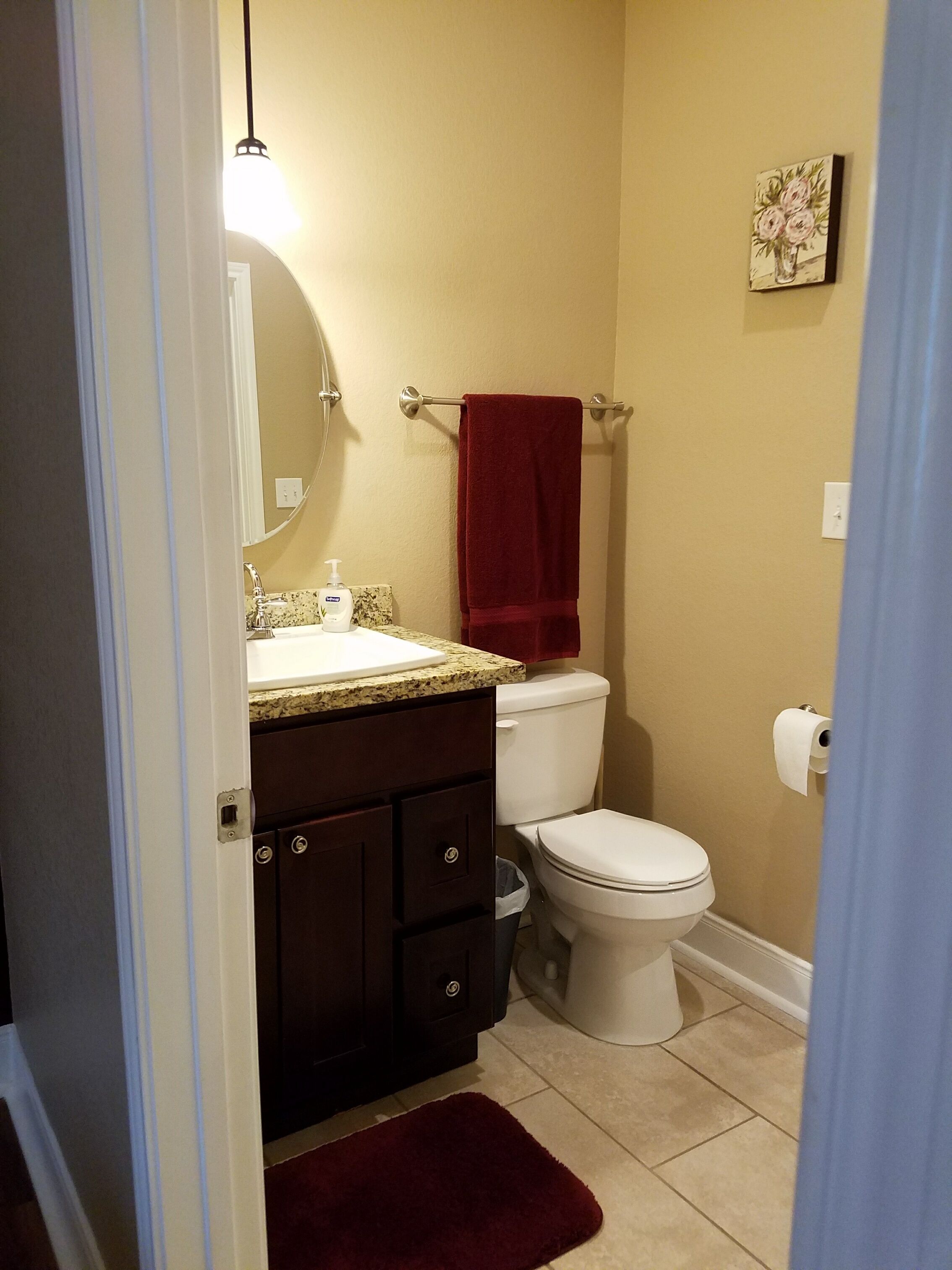 A bathroom with a white toilet, a dark wood vanity, a red towel, and a beige wall.
