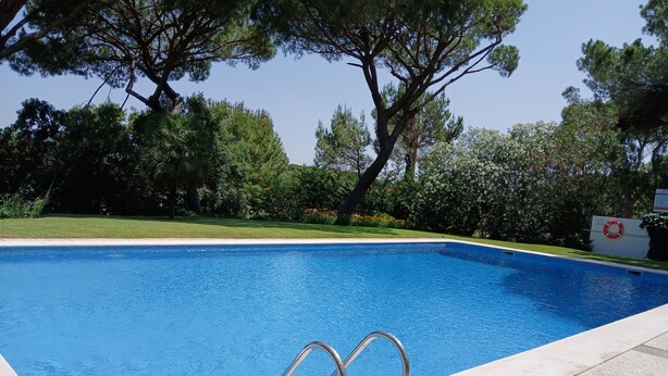 A clear blue swimming pool with metal handrails, surrounded by lush greenery and trees. - Beautiful Townhouse for golfers and beach holidays in sunny Vilamoura (Vilamoura)