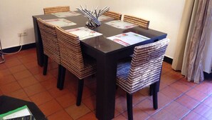A dining area with a table set for four, surrounded by wicker chairs, a painting on the wall, and a curtain on the window. - Beautiful Townhouse for golfers and beach holidays in sunny Vilamoura (Vilamoura)