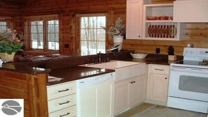 A wooden cabin-style kitchen with a large island, white cabinetry, and a white stove. - Homestead Hideaway away from it all (Glen Arbor)