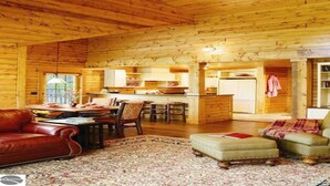 A cozy log cabin interior with a dining area, a living room with a leather sofa, and a kitchen with white cabinets. - Homestead Hideaway away from it all (Glen Arbor)