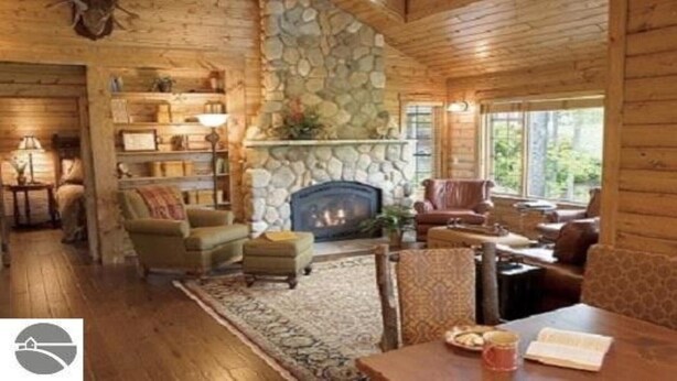 A cozy log cabin interior with a stone fireplace, wooden furniture, and a bookshelf. - Homestead Hideaway away from it all (Glen Arbor)
