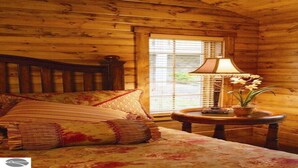 A wooden cabin room with a bed, a window with blinds, a lamp, and a potted plant. - Homestead Hideaway away from it all (Glen Arbor)