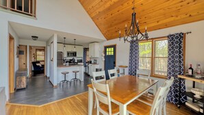 A spacious kitchen with modern appliances, a dining area with a wooden table and chairs, and a view through large windows.
