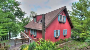 A red house with a wooden deck and a staircase leading to the entrance.