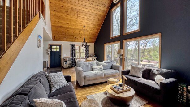 A spacious living room with a high ceiling, a staircase, and large windows.