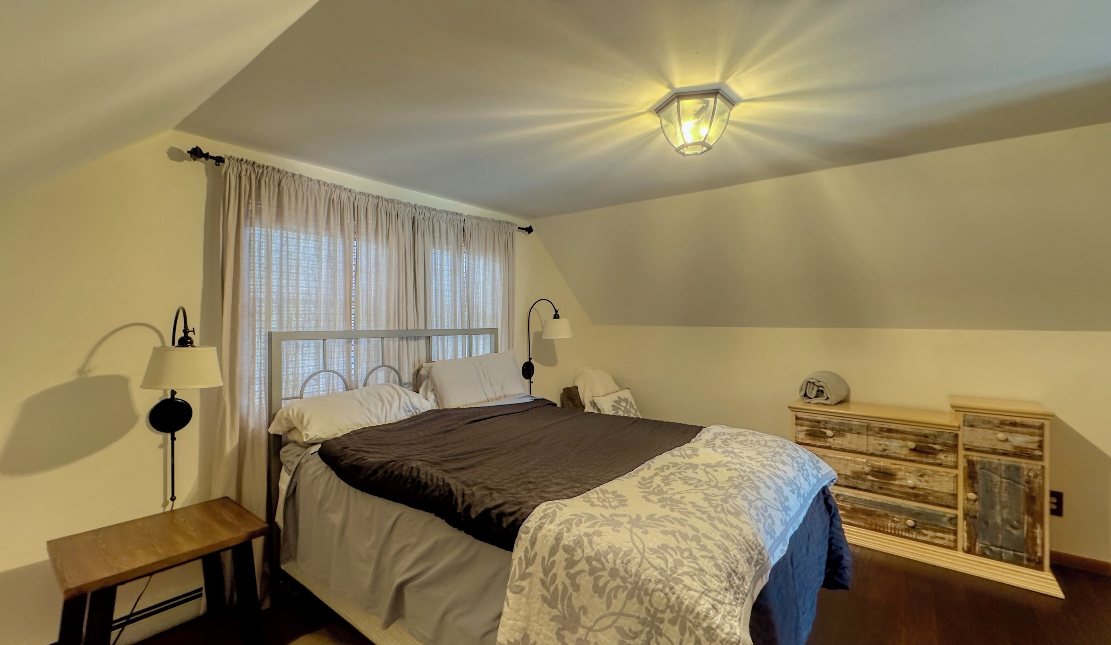 Ein Schlafzimmer mit einem Bett, zwei Nachttischlampen, einem Nachttisch, einer Kommode und einer Deckenleuchte.