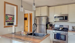 A modern kitchen with stainless steel appliances, wooden countertops, and a hanging light fixture.