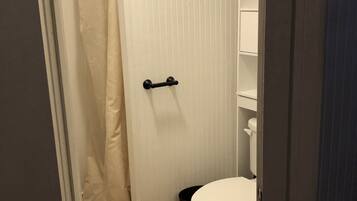 A small, compact bathroom with a white toilet, a black trash bin, and a shower curtain.
