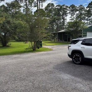 A gravel driveway leading to a building with a covered area, surrounded by trees and a white vehicle parked nearby. - The Shed on MonLouis Island with nearby fishing docks (Coden)