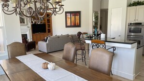 Een moderne keuken met een centraal eiland, een eethoek met een houten tafel, en een woonkamer met een bank en een open haard.