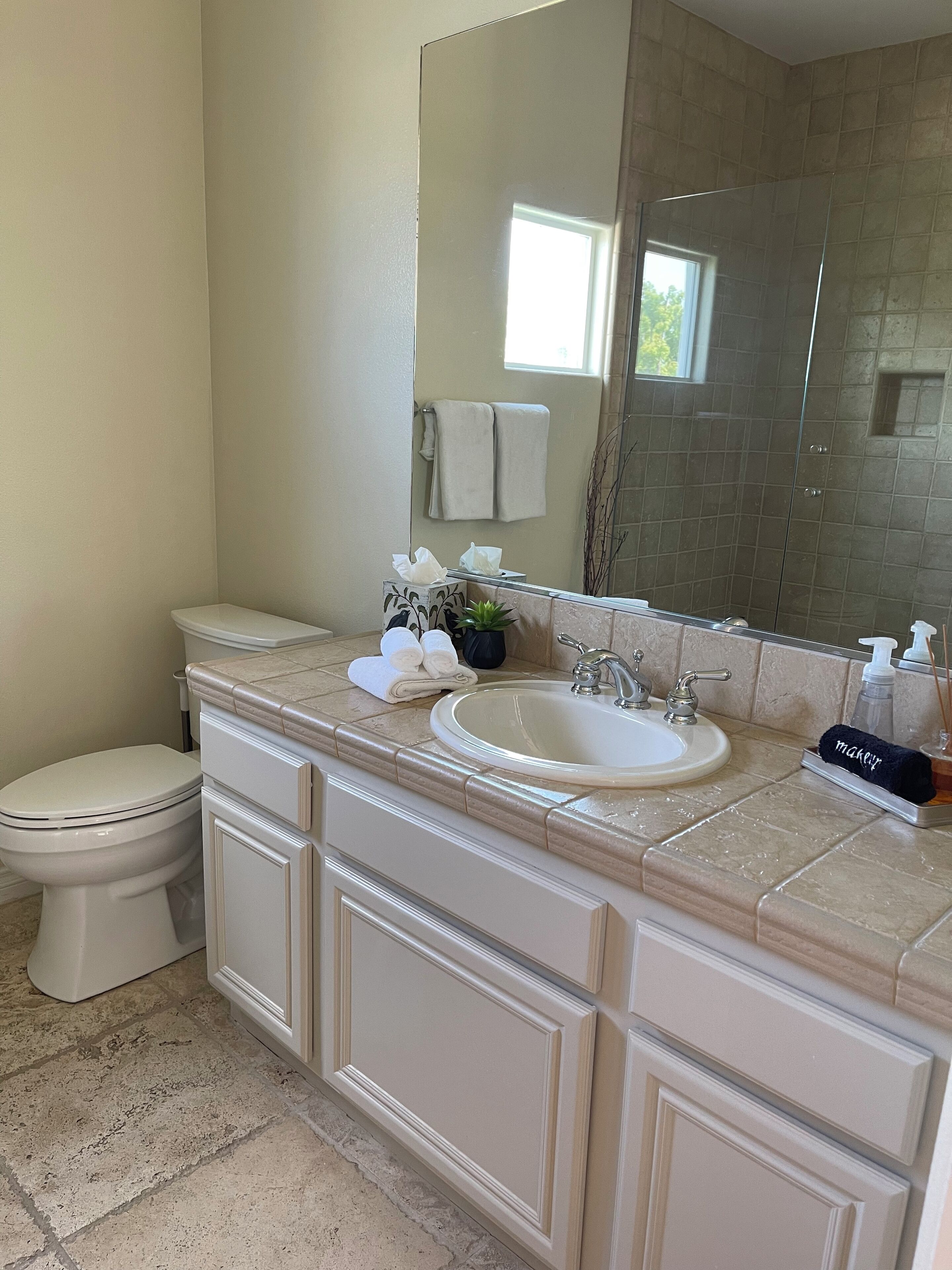 A bathroom with a toilet, sink, and mirror. There are towels and toiletries on the counter.