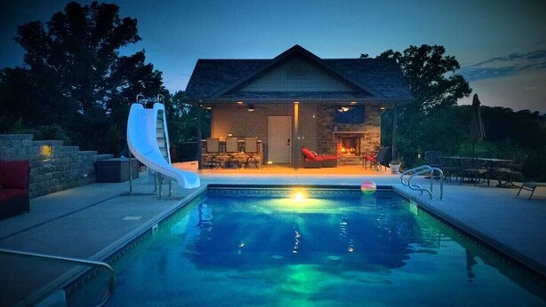 A swimming pool with a slide, a stone building with a door, and outdoor seating. - Scenic Lakeside Chateau with Heated Pool, Hot Tub & Outdoor Kitchen-TV-Fireplace (Belle)