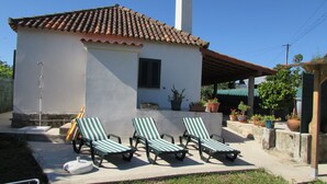 Una casa con techo de tejas, un porche cubierto con tres sillones a rayas y plantas en macetas.