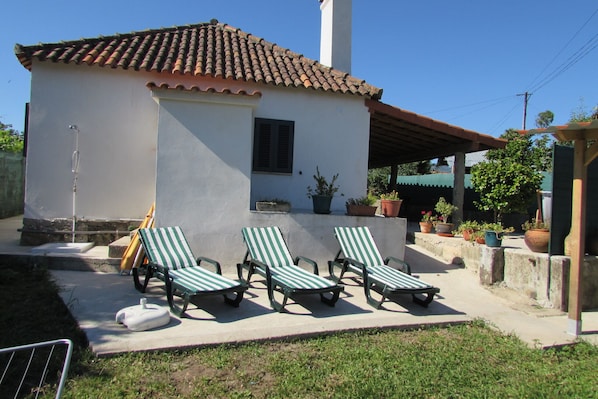 A house with a tiled roof, a covered patio with three striped lounge chairs, and potted plants.