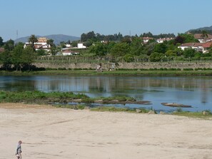 A river with a sandy bank and a few trees. In the background, there are houses and a stone wall. - Local tourism - Casas da Nazare - Ponte de Lima (Ponte de Lima)