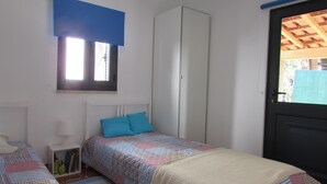 Un dormitorio con dos camas, un armario, una ventana con persianas y una puerta que da al exterior.