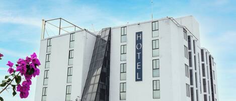 A modern hotel with a prominent 'HOTEL' sign, a parking area, and a visible storefront with a red and white sign.