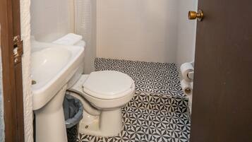 Un baño con inodoro blanco, lavamanos, ducha con cortina y baldosas de suelo estampadas.
