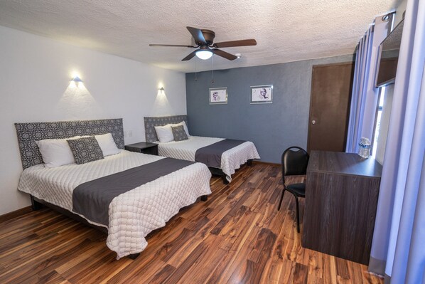 A hotel room with two beds, a desk, a chair, a ceiling fan, and wall-mounted lights. - Hotel Delf-inn (Jiutepec)