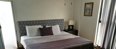 A neatly made bed with a patterned headboard, a bedside table with a lamp, and a window with curtains.