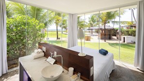 Un baño moderno con un ventanal grande, un tocador de madera, un lavabo tipo cuenco y una cama con toallas.