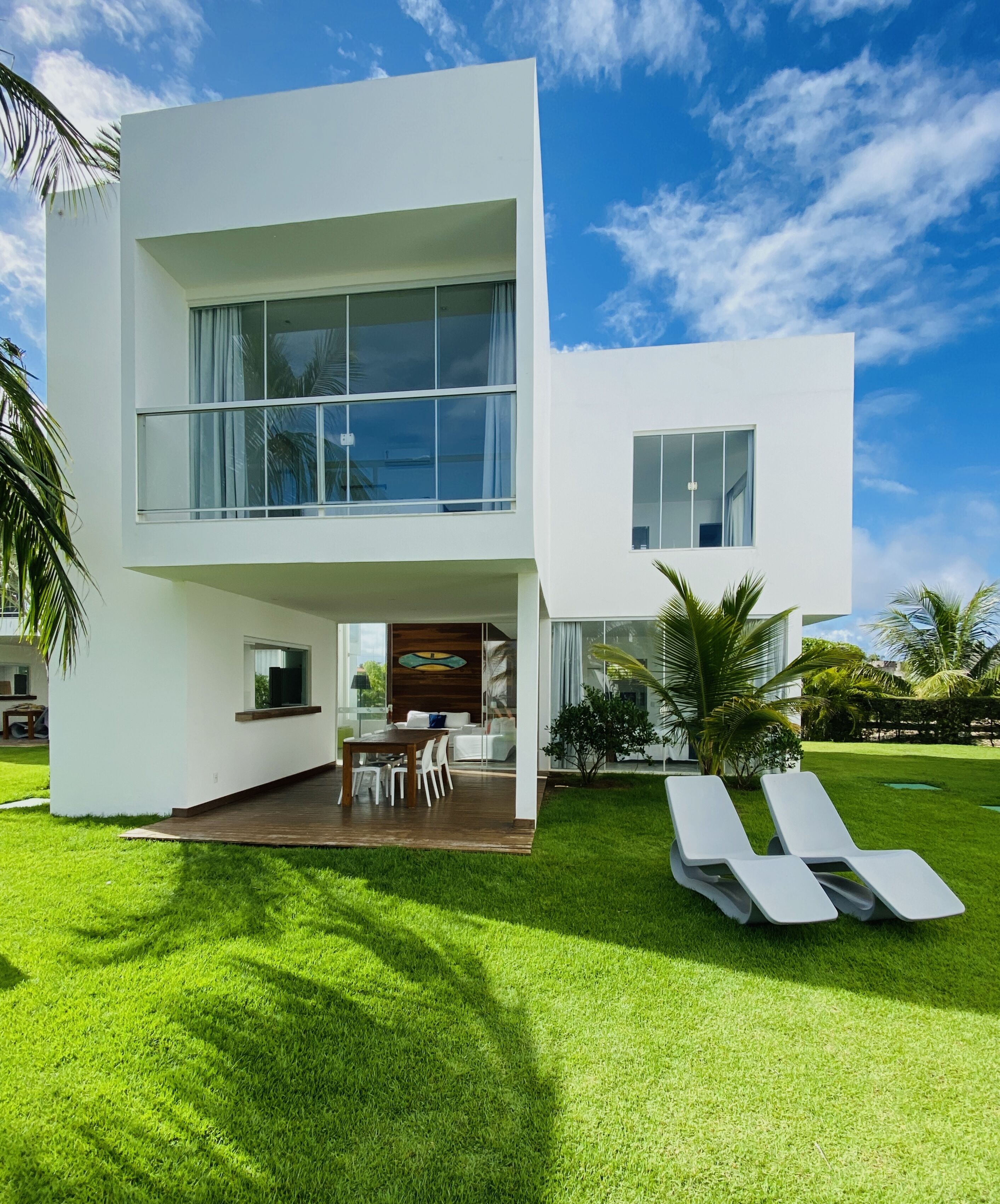 A modern two-story house with a large balcony, a dining area, and a well-maintained lawn.