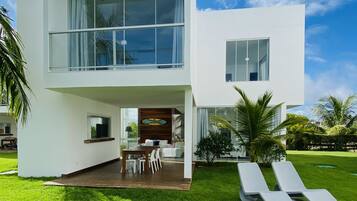 A modern two-story house with a large balcony, a dining area, and a well-maintained lawn.