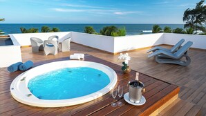 Zona de piscina en la azotea con jacuzzi, sillones de descanso y una mesa con champán y copas.