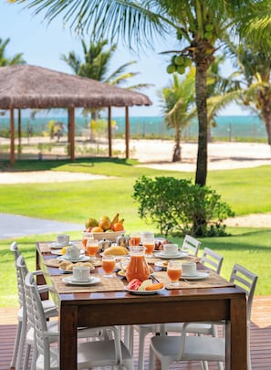 A dining table set outdoors with a view of a beach and palm trees.